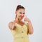 Portrait of young woman showing double thumbs up in yellow dress and looking happy front view